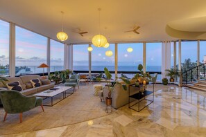 A spacious living area with a large window overlooking the sea, a sofa, chairs, a coffee table, and potted plants. - Pestana Carlton Madeira Ocean Resort Hotel (Funchal)