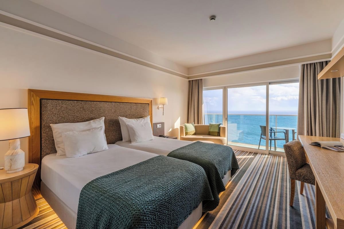 Habitación de hotel con dos camas, un escritorio, una silla y vista al océano.