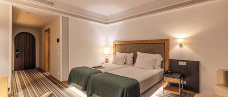 Una habitación de hotel con una cama, dos mesitas de noche, una silla, una lámpara y una puerta que da a un pasillo.