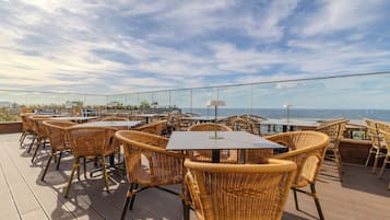 Terraço no telhado com cadeiras e mesas de vime, com vista para a costa.