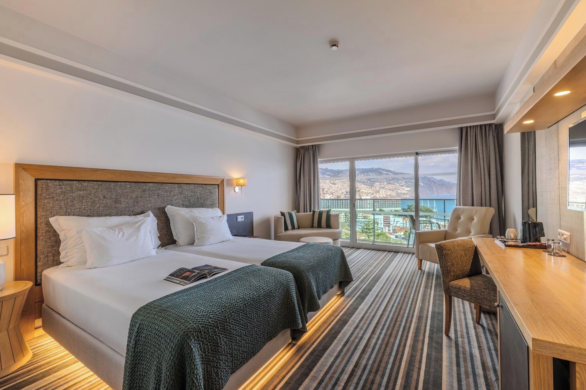Una camera d'albergo con un letto grande, due comodini, una scrivania, una sedia e vista sulla città.