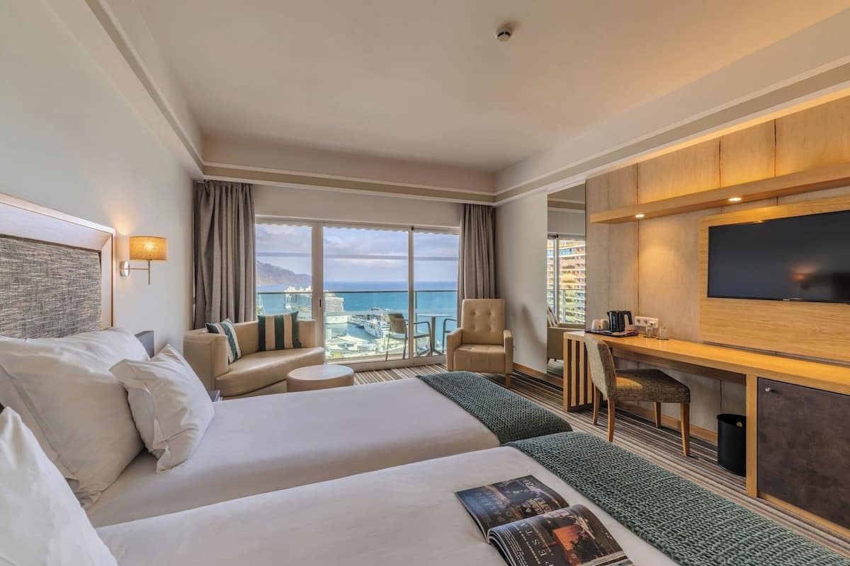 Habitación de hotel con dos camas, un escritorio, un televisor y vista al océano.