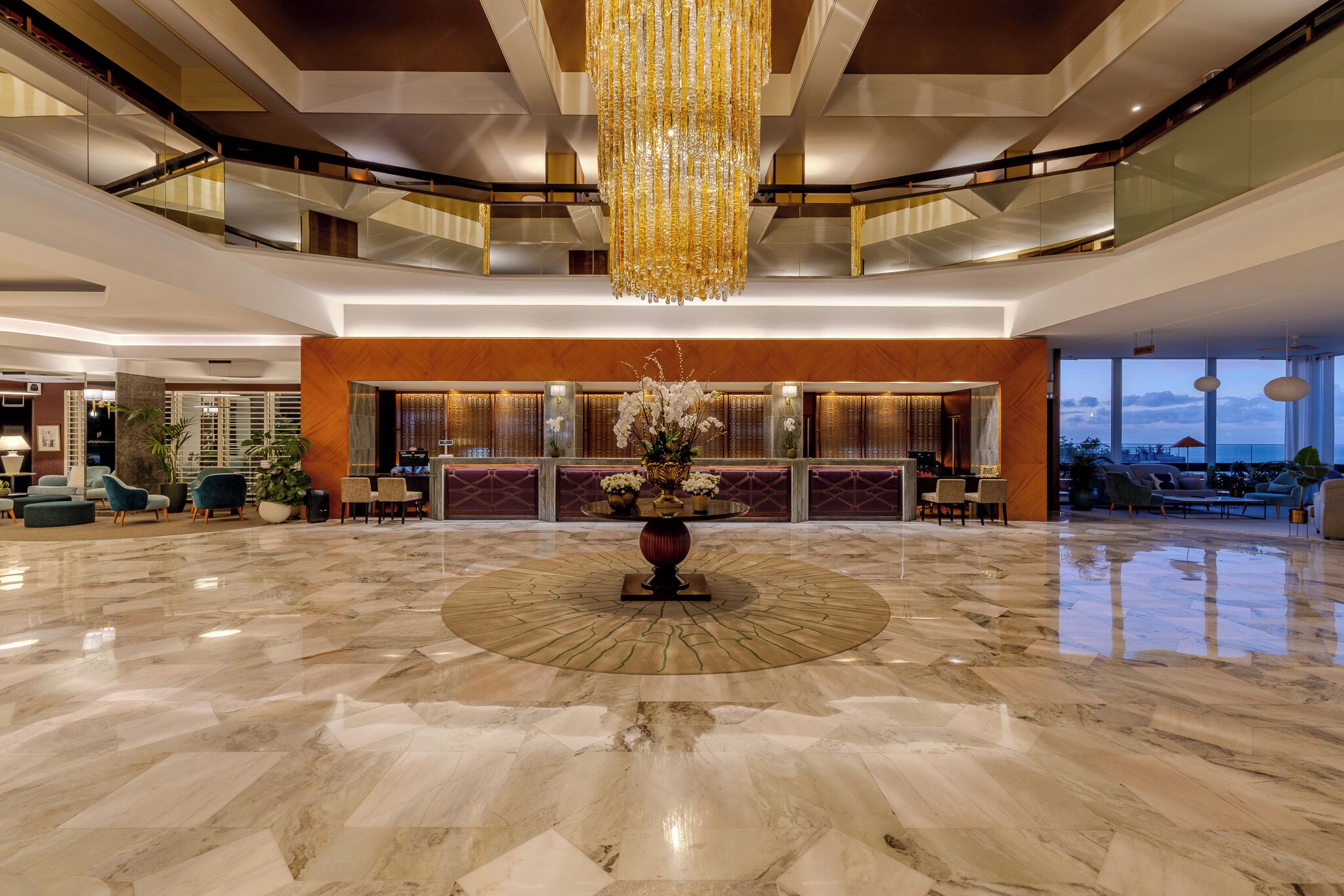 Un amplio vestíbulo con una fuente decorativa en el centro, un gran candelabro y un moderno mostrador de recepción.