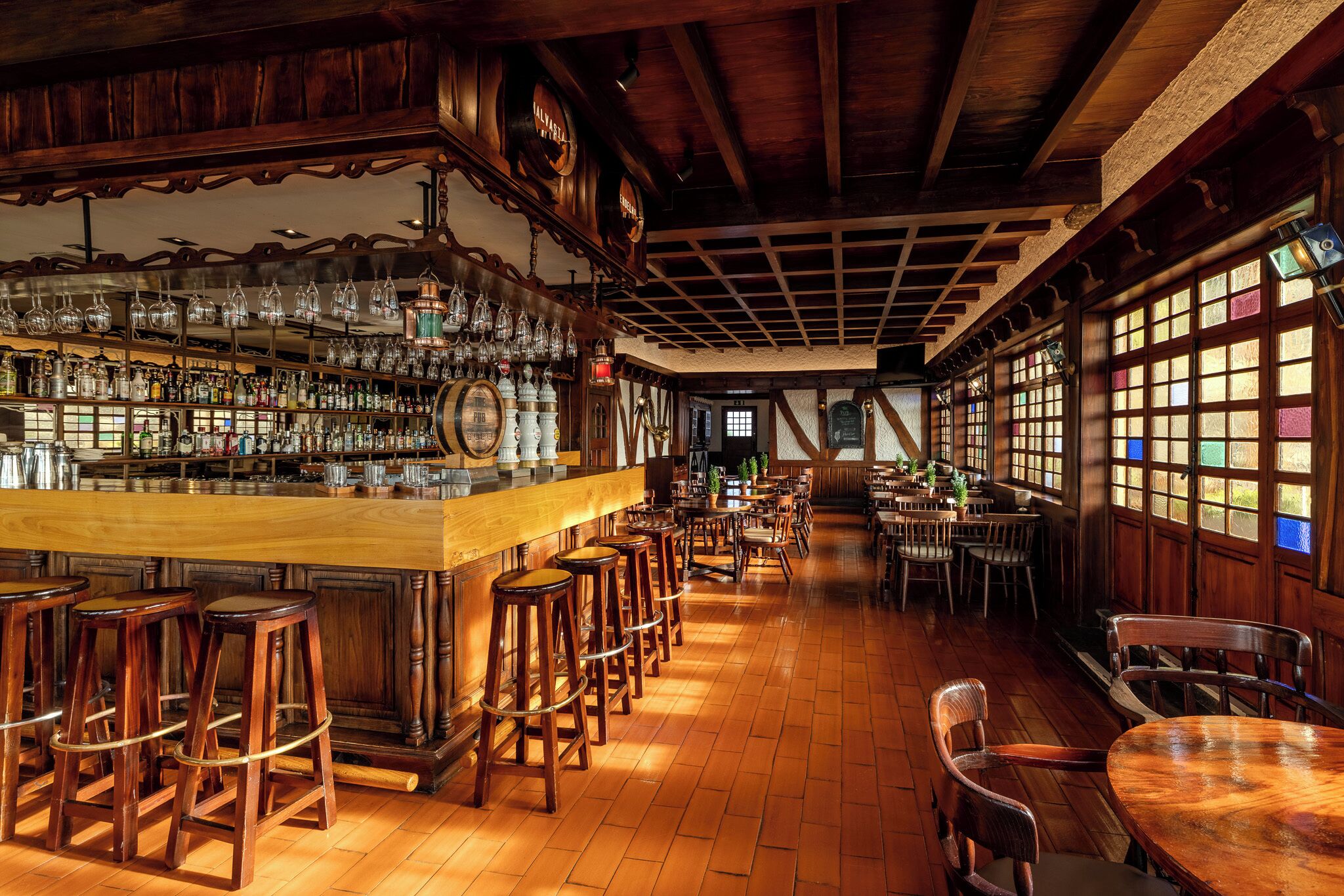 A bar area with wooden stools, a bar counter, and shelves with bottles.