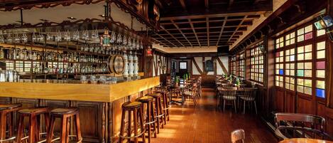 A bar area with wooden stools, a bar counter, and shelves with bottles.