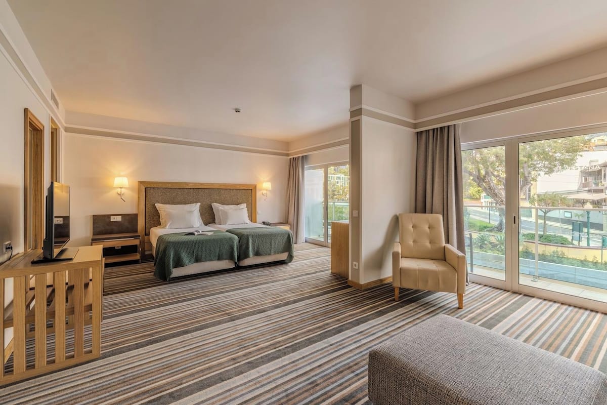 Habitación de hotel con cama, una silla, escritorio, televisor y ventana grande.