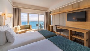 Une chambre d’hôtel avec deux lits, un bureau, une télévision et une vue sur la mer.