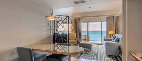 A modern hotel room with a dining area, a sofa, and a view of the sea.