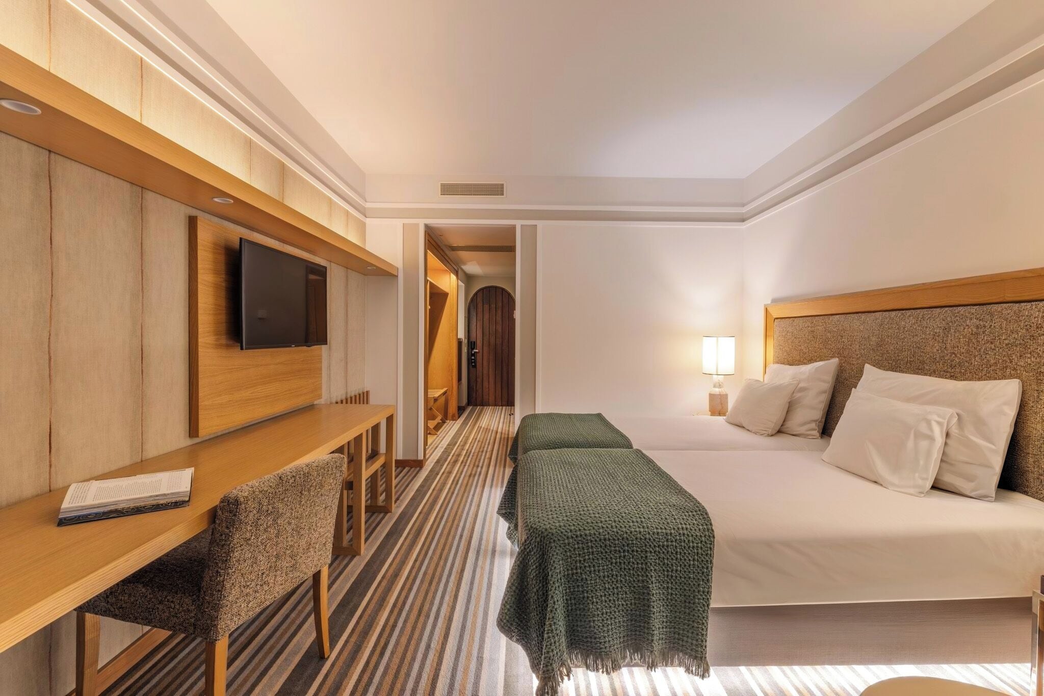 Ein Hotelzimmer mit einem Bett, einem Schreibtisch mit Stuhl, einem Fernseher und einer Lampe.