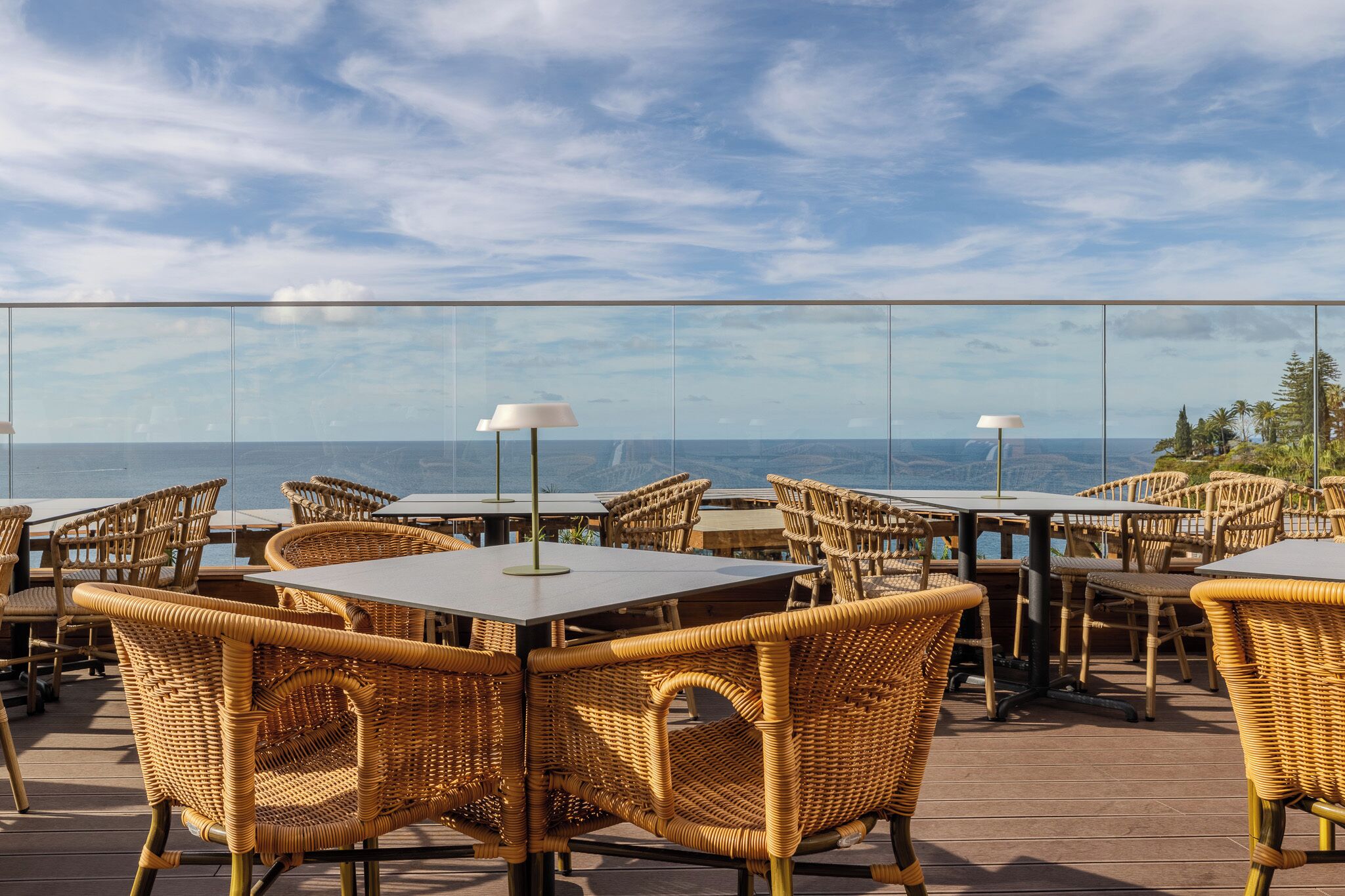 Outdoor dining area with wicker chairs and tables, overlooking a scenic view.