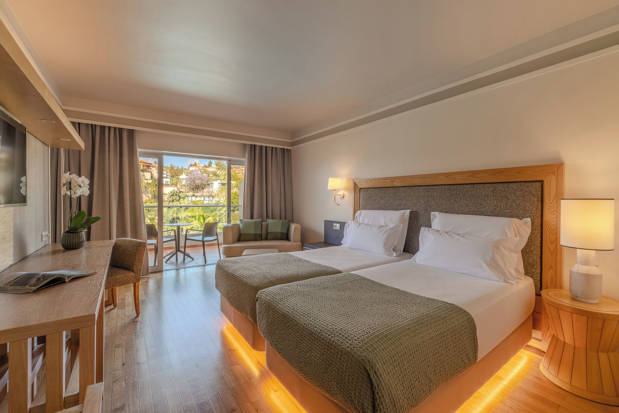 A hotel room with a bed, bedside tables, a desk, and a view of the outdoors.