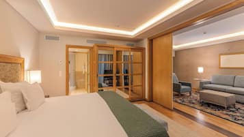 Ein Hotelzimmer mit einem Bett, einer Sitzecke mit einer Couch und Sesseln sowie Blick ins Badezimmer durch eine Glastür.