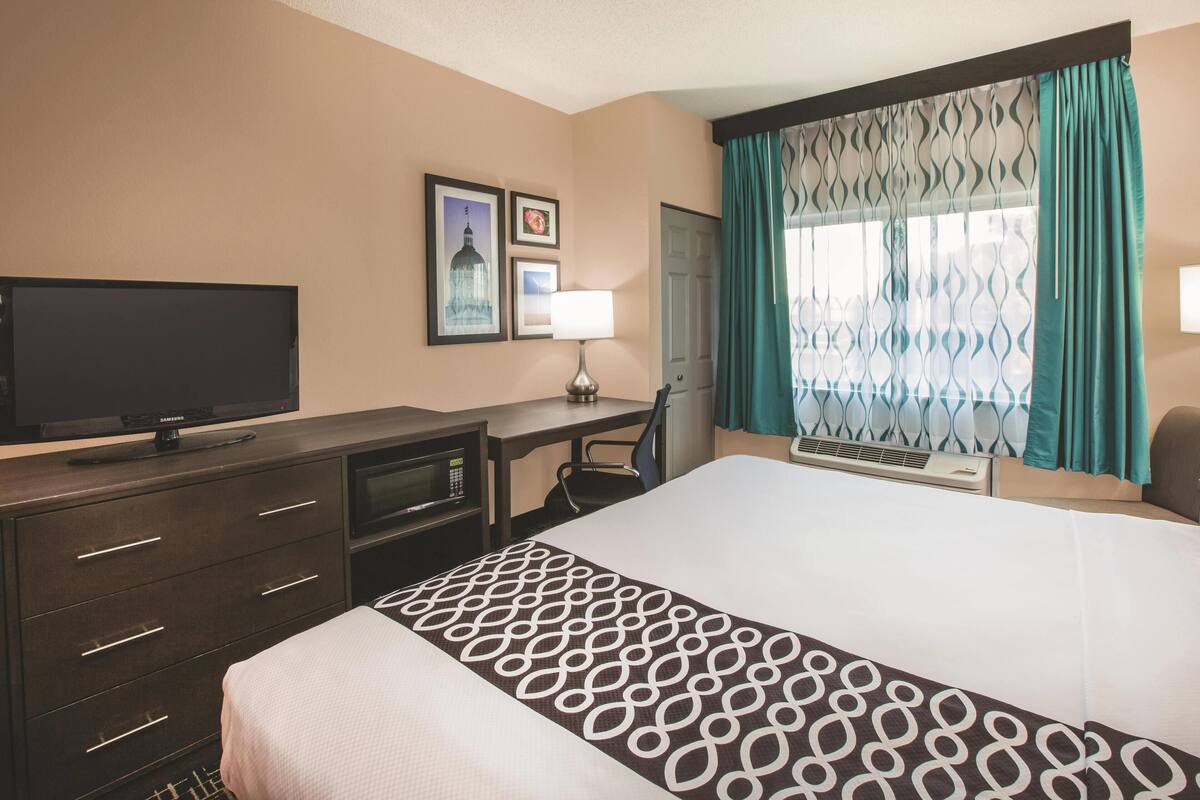A hotel room with a bed, a desk with a computer, a television, and a window with curtains.