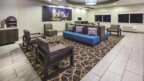 A hotel lobby with a blue sofa, seating area, and a reception desk. - La Quinta Inn by Wyndham Indianapolis North at Pyramids (Indianapolis)
