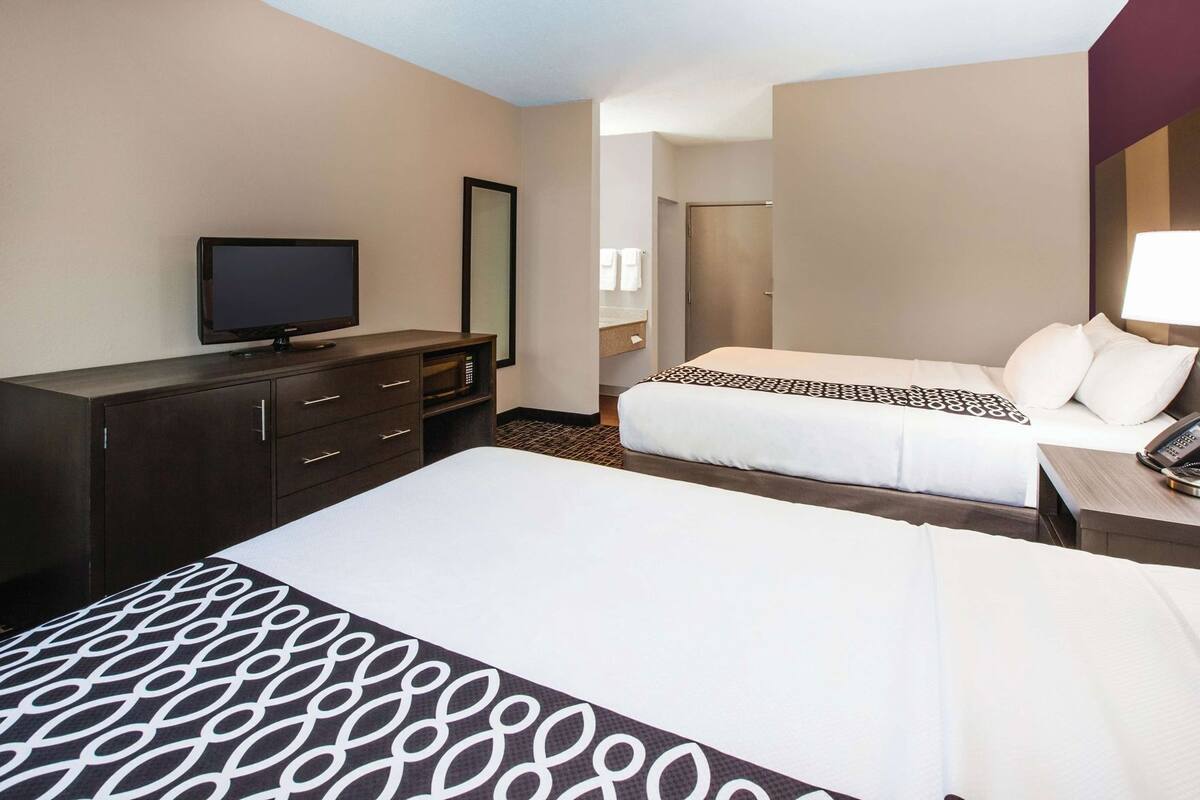 A hotel room with two beds, a TV, a dresser, and a bathroom visible through an open door.