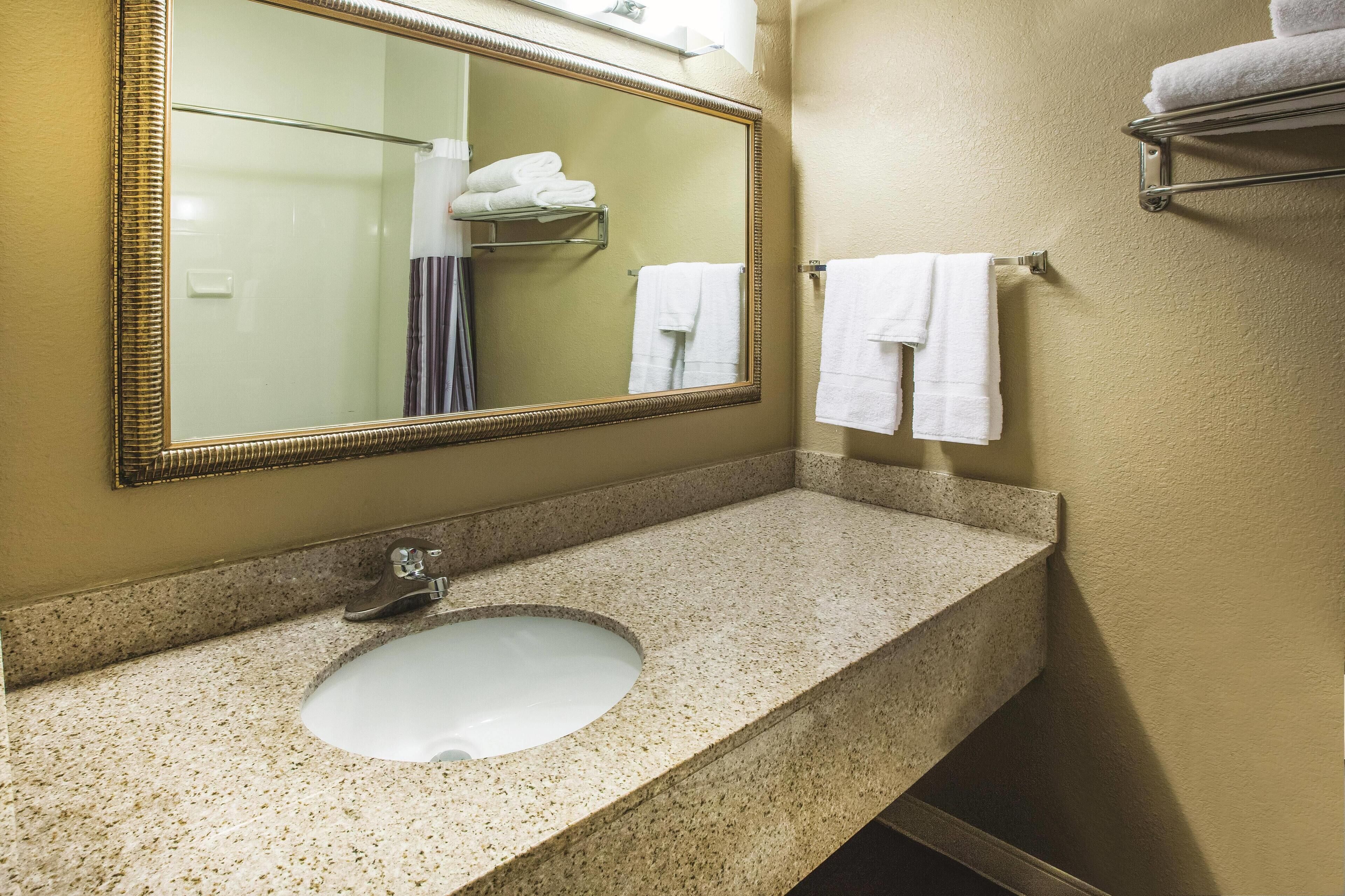 Une salle de bain dotée d’un comptoir en granit, d’un lavabo, d’un miroir et d’un porte-serviettes avec des serviettes pliées.