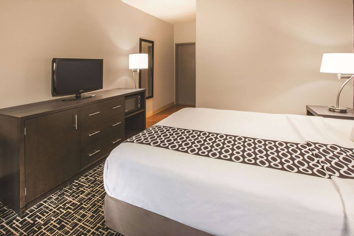 A hotel room with a bed, a TV on a dresser, a lamp, and a patterned rug.