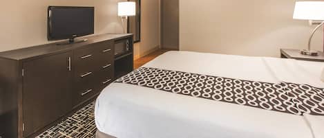 A hotel room with a bed, a television on a dresser, a mirror, and a nightstand with a lamp.