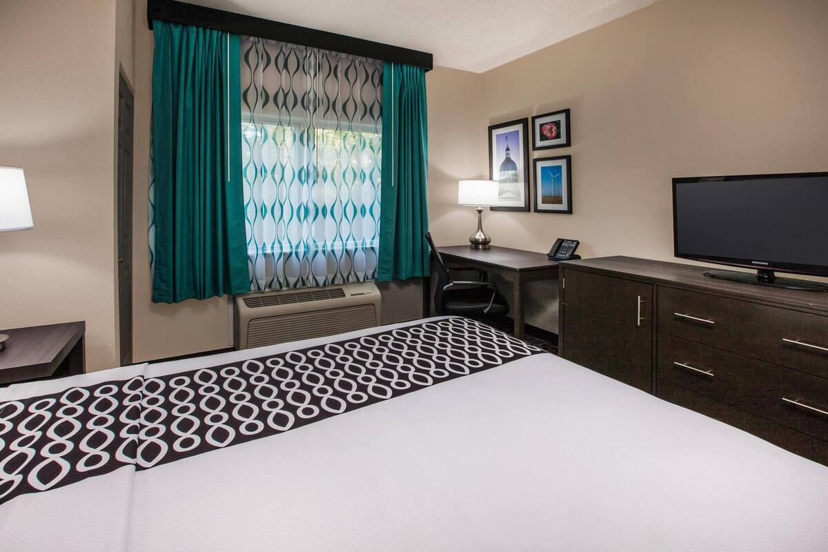 A hotel room with a bed, desk, chair, TV, and a window with curtains.