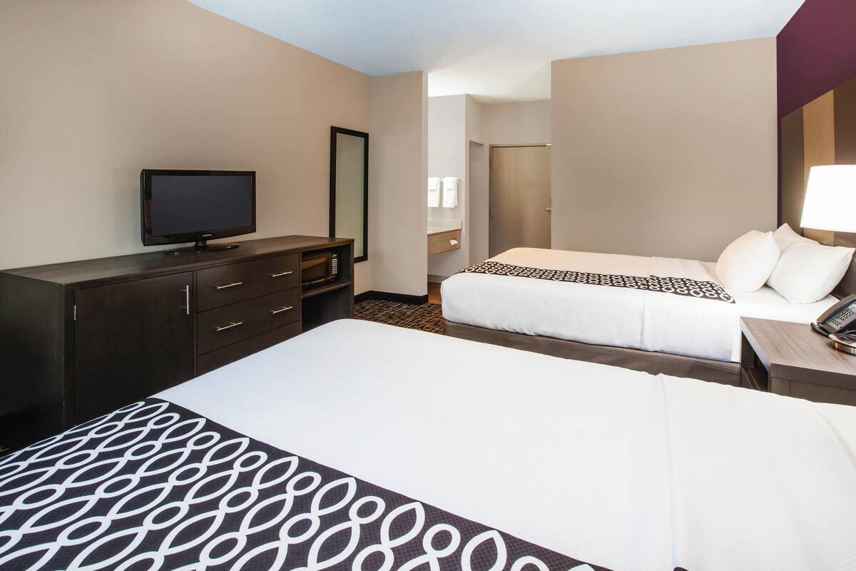 A hotel room with two beds, a TV, a dresser, and a mirror.