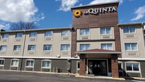A La Quinta hotel with a modern design, featuring a prominent sun logo, multiple windows, and a parking lot in front. - La Quinta Inn by Wyndham Indianapolis North at Pyramids (Indianapolis)