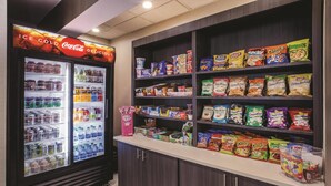 A snack and beverage display area with a Coca-Cola refrigerator and shelves stocked with various snacks like Lay's and Smartfood. - La Quinta Inn by Wyndham Indianapolis North at Pyramids (Indianapolis)