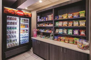 Uma área de exposição de lanches e bebidas, com um refrigerador Coca-Cola e prateleiras repletas de diversos salgadinhos, como Lay's e Smartfood.