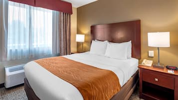 A hotel room with a large bed, a nightstand with a lamp, a phone, and a digital clock.