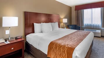 A hotel room with a large bed, a wooden headboard, two bedside lamps, a desk with a telephone, and a window with curtains.