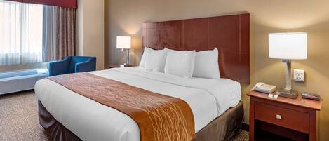 A hotel room with a large bed, two bedside tables, a desk, a chair, and a window with curtains.