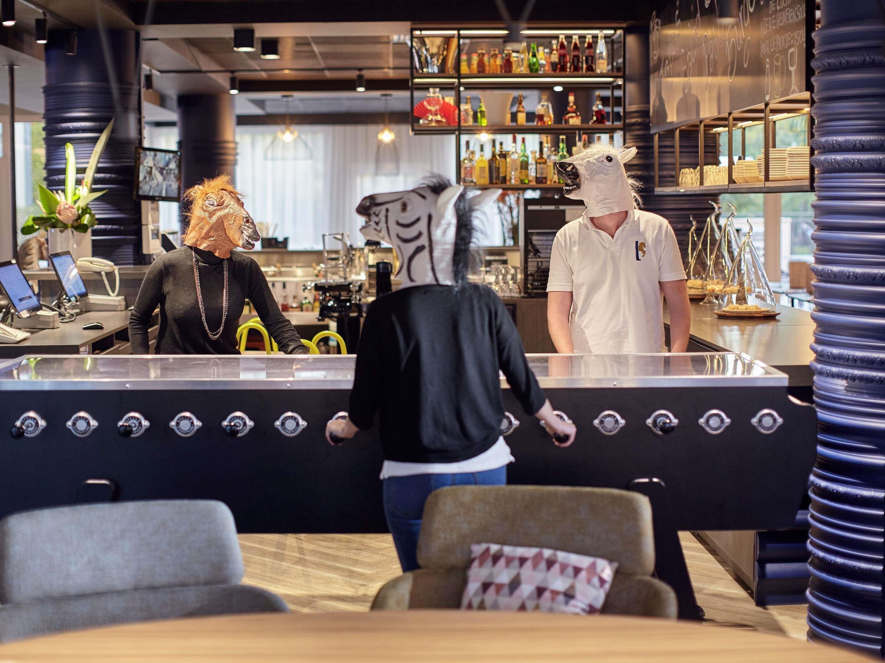 Eine Bar mit einer Theke, Hockern und einer Person mit Pferde-Maske.