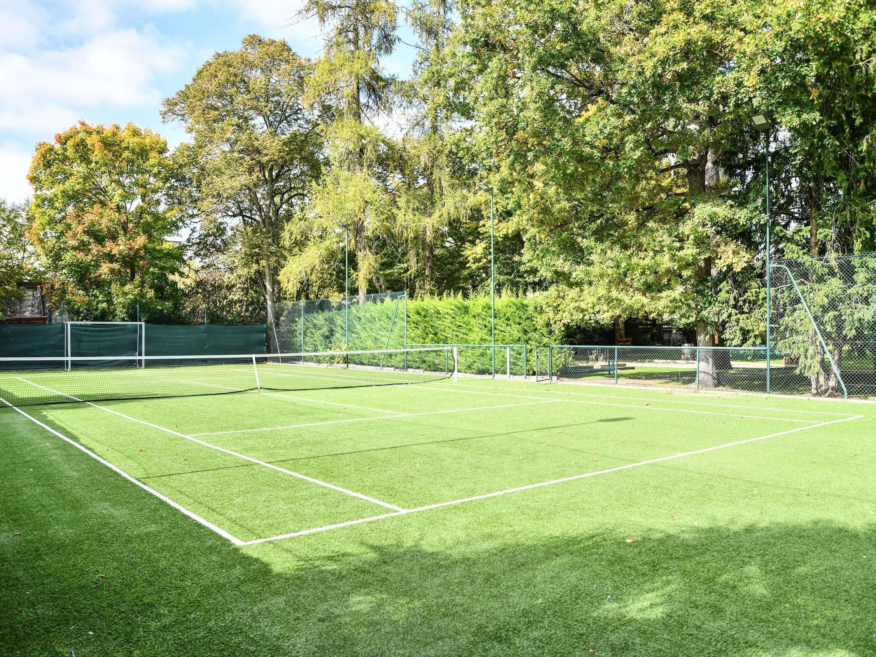 A tennis court with a net, surrounded by trees and a fence.