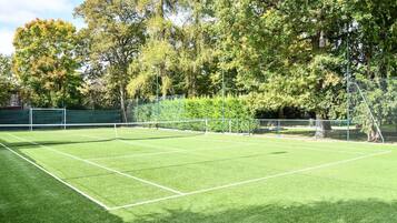 A tennis court with a net, surrounded by trees and a fence.