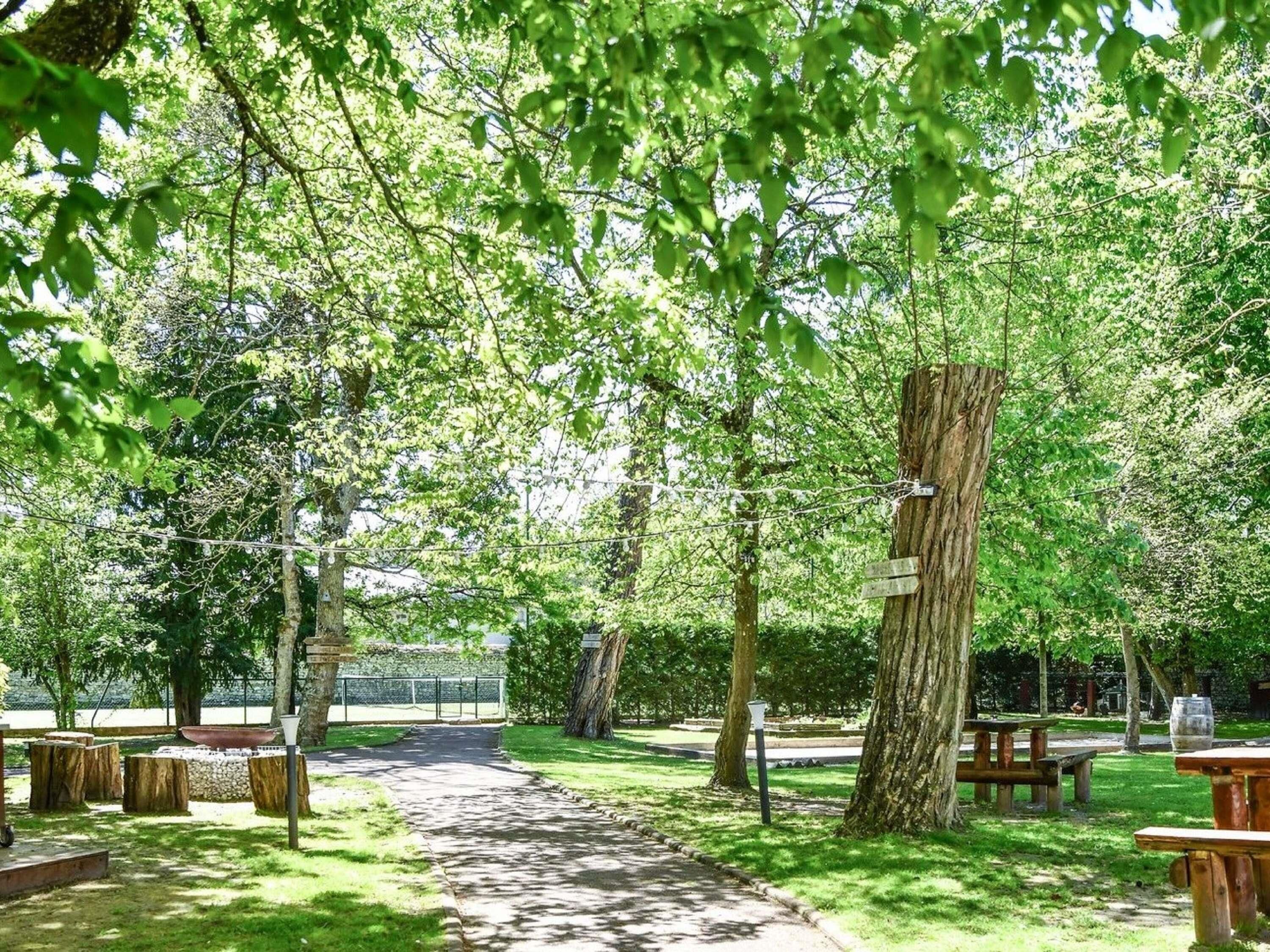Un parque con un sendero pavimentado, bancos de madera y mesas para picnic.