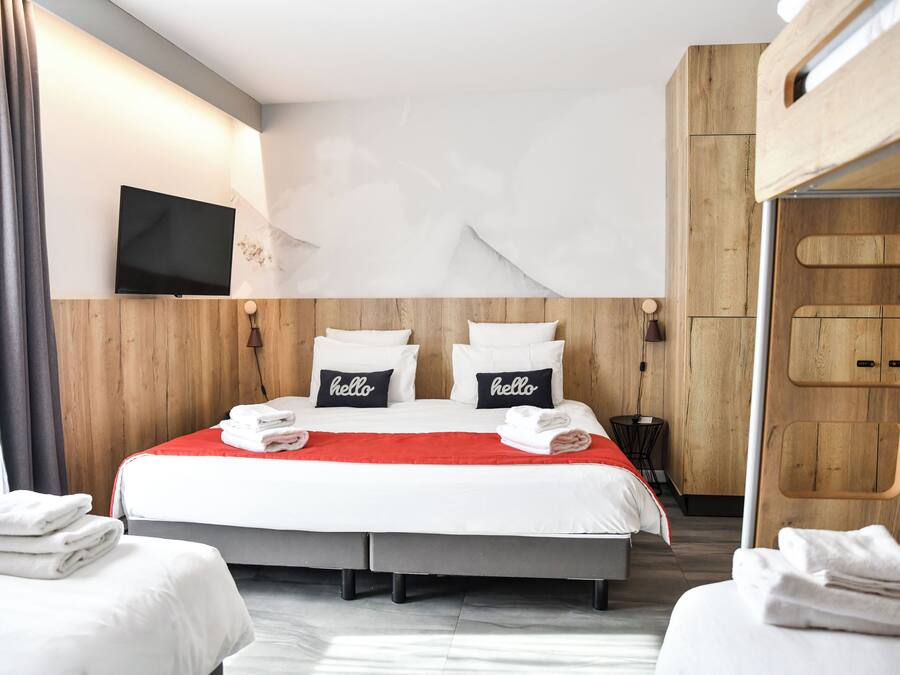 Ein Hotelzimmer mit einem großen Bett, zwei Kissen mit "hello"-Aufzug, einem an der Wand montierten Fernseher und einem Holzschrank.