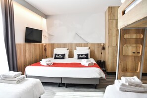 Een hotelkamer met een groot bed, twee kussens met de tekst 'hello' en een aan de muur bevestigde televisie, plus een houten garderobe.