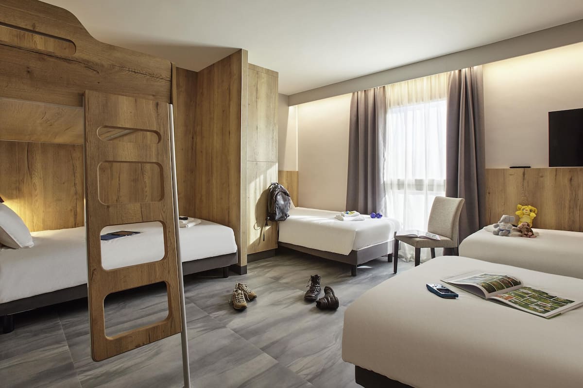 A hotel room with a bunk bed, a single bed, a chair, a desk, and a TV.
