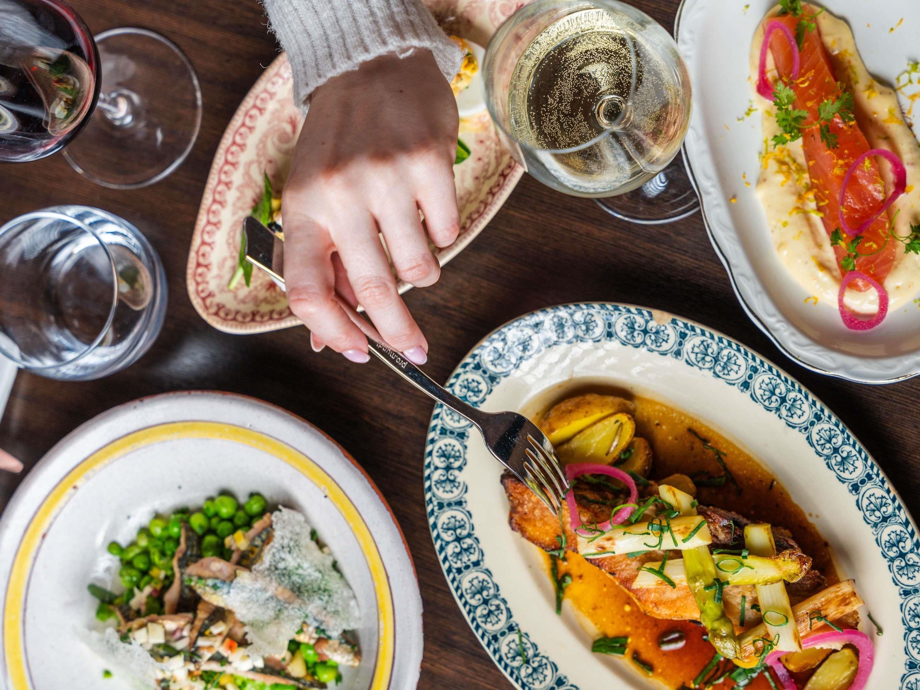 Une table à manger avec différents plats, une main tenant une fourchette et des verres de vin.