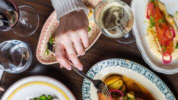 Une table à manger avec différents plats, une main tenant une fourchette et des verres de vin.