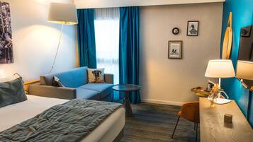 Een hotelkamer met een bed, een slaapbank, een kleine tafel, een bureau, een lamp en uitzicht op de omgeving.