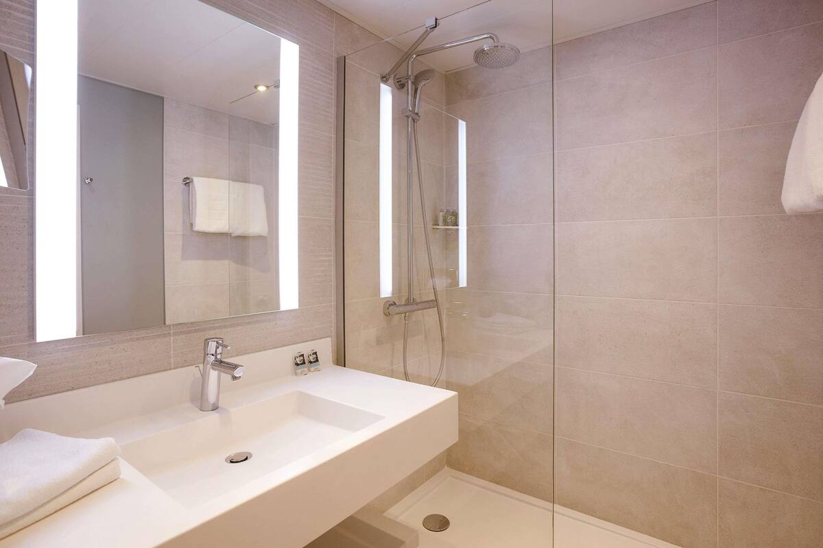 A modern bathroom with a large mirror, a sink, and a glass-enclosed shower.