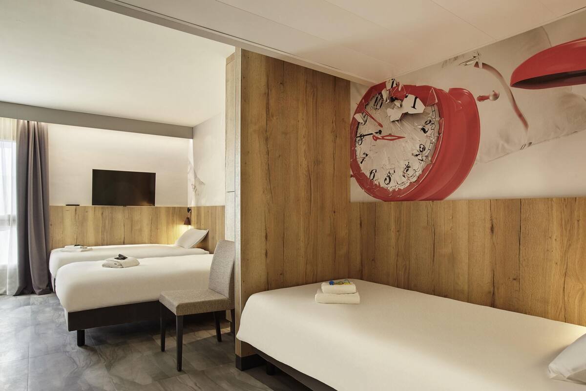 A hotel room with two beds, a wooden headboard, a large clock on the wall, and a flat-screen TV.