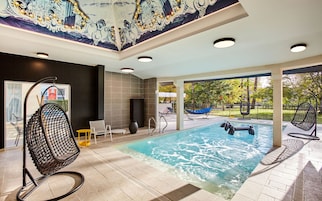 A modern indoor pool area with a clear view of the outdoors, a seating area with chairs, and a decorative ceiling mural.
