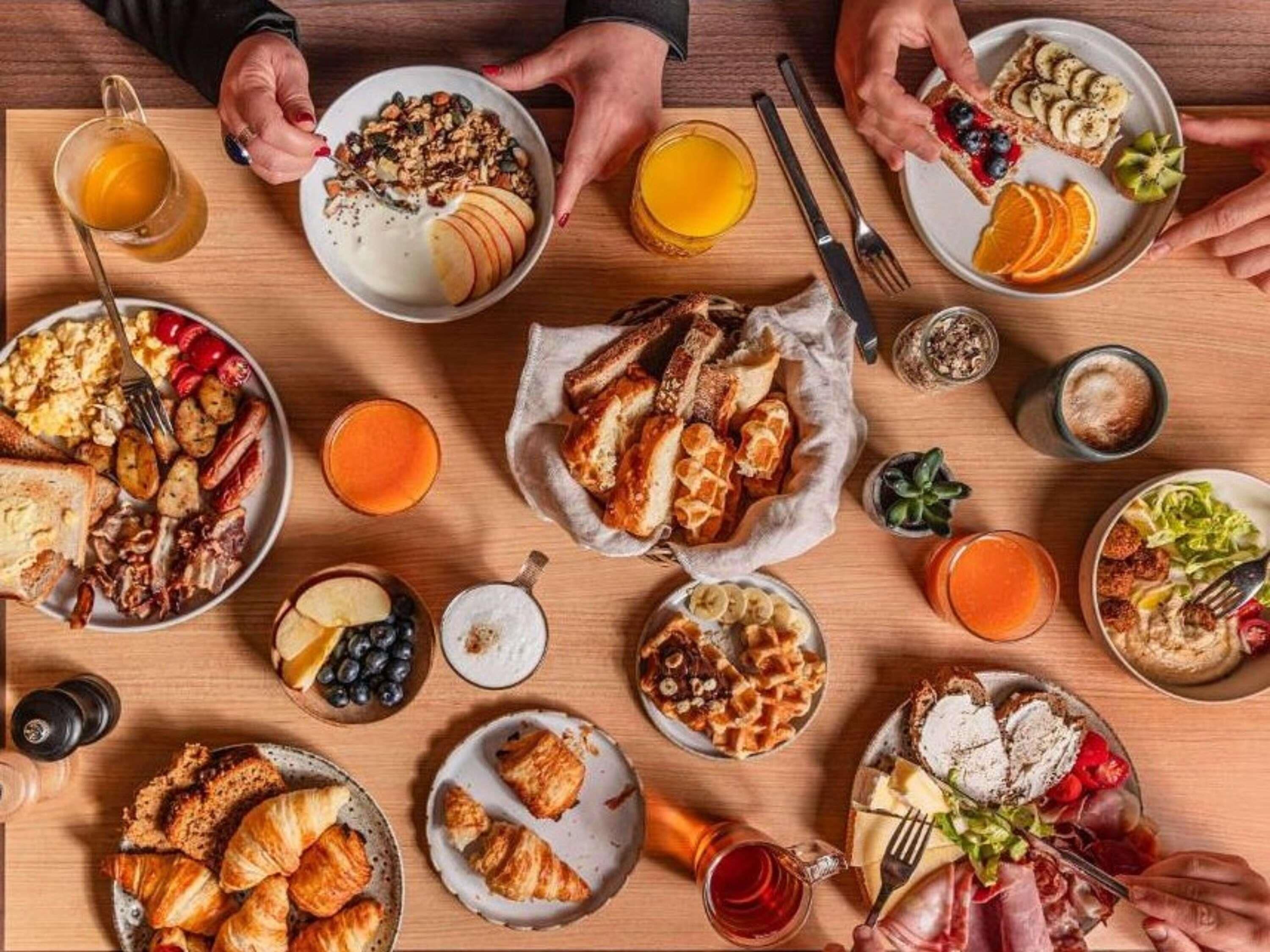 Un bufé de desayuno con diversos platos, bebidas y utensilios sobre una mesa de madera.
