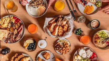 A breakfast buffet with various dishes, drinks, and utensils on a wooden table.