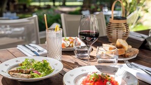 A dining table set outdoors with plates of food, a glass of red wine, and a basket. - Demeures de campagne Château de Fontainebleau – Mercure (Fontainebleau)