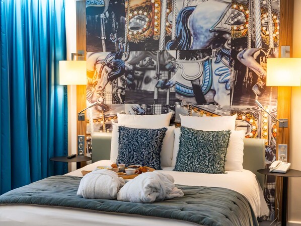 Une chambre d’hôtel avec un lit, deux oreillers, une table de chevet avec une lampe et un mur orné d’une fresque.