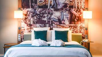 A hotel room with a large tapestry on the wall, a bed with white and green bedding, two bedside lamps, and a small table with a phone.
