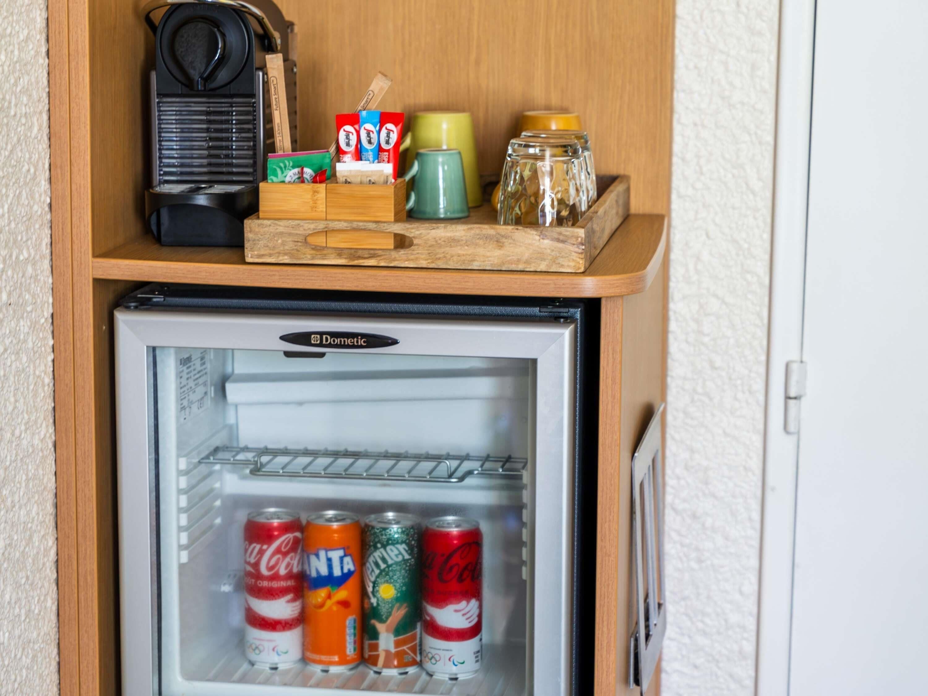A mini-fridge with a few cans of soda, a coffee maker, and a jar on top.