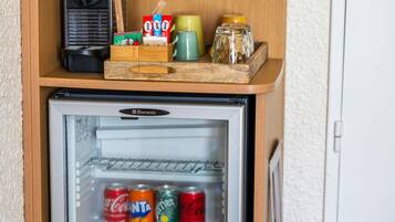 A mini-fridge with a few cans of soda, a coffee maker, and a jar on top.